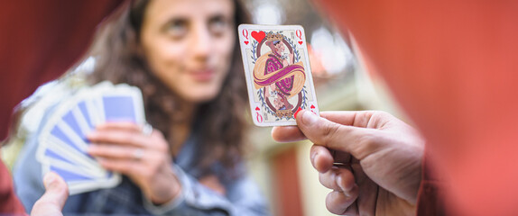Card playing in a spring garden: Couple are sitting on a table, relaxing and playing cards together. Blurry background.