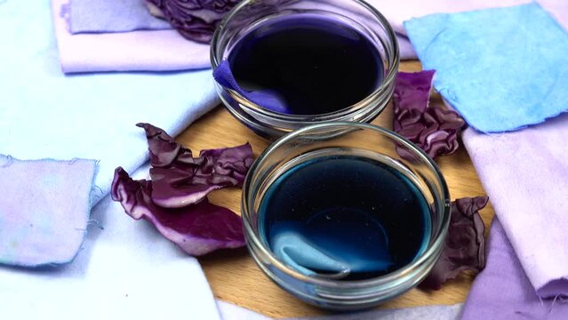 Bowls with decoction of red cabbage and samples of cotton fabric with gradient in blue and pale purple tones, background.  Natural dyeing for fabrics, DIY