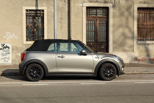 Udine, Italy. February 4, 2023. Gray convertible Mini Cooper in a city street with abandoned old house on background 