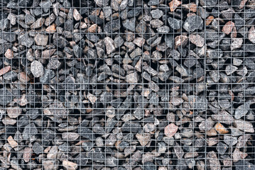 Stone wall made of whetstone in light gray, enclosed behind a metal mesh. Mineral surface without mortar joints. Construction of an old house and a park.