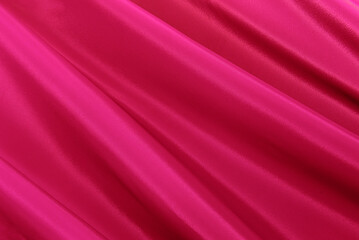 Texture of a smooth luxurious, elegant fabric in burgundy, purple, red. Purple satin or silk fabric with folds and waves