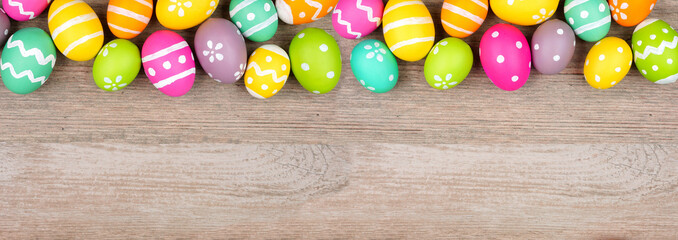 Colorful Easter egg top border. Overhead view on a light wood banner background. Copy space.