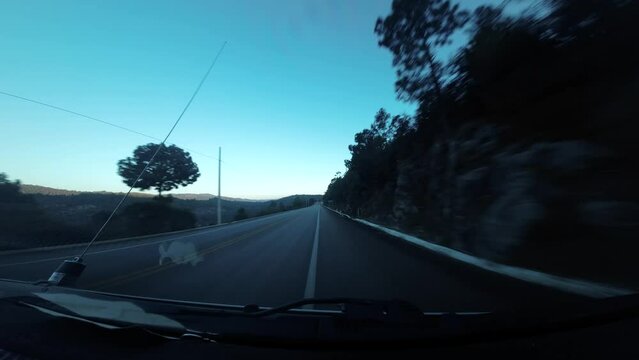 Viajando por la carretera entre monta&ntilde;as y arboles, se observa hermosas vistas mientras se viaja en el atardecer azul.