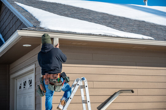 Contractor installing gutters on a residential building in the winter with snow on the roof.