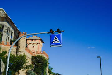 A pedestrian crossing road sign on the background of a blue sky and a medieval castle next to the...