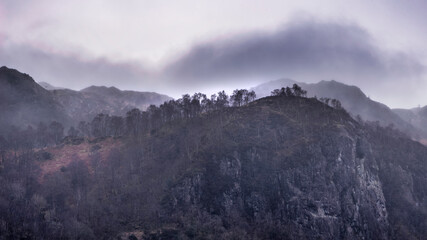 Lovely calm Winter morning landscape image of view of a fog shrouded crag above Derwent water