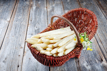 Frischer roher weißer Spargel mit Kräutern und Blumen angeboten als close-up in einem Korb auf...