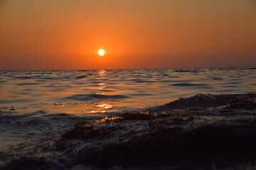 Obraz premium Vibrant sunset descending on the horizon, sea in golden colors, small waves gently touching the sands,