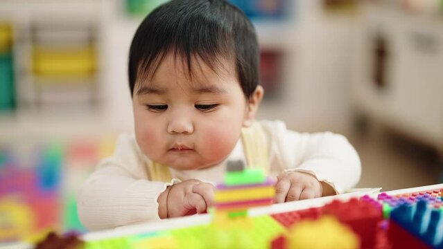 Adorable hispanic baby playing with construction blocks sitting on table at kindergarten