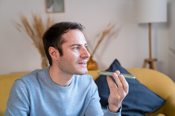 Young man using smartphone at home sending a voice note