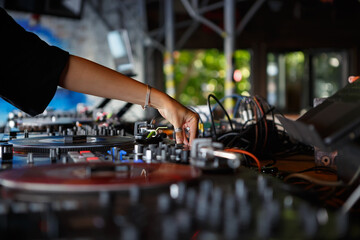 Female DJ plays techno music with vinyl turntables on party in a bar. Hands of young woman mixing records on stage