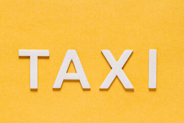 Word TAXI, in wooden letters on yellow background