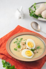 Polish Easter soup Zurek with white sausages and a boiled egg in a green ceramic bowl on a light concrete background. Traditional Polish Easter dishes.