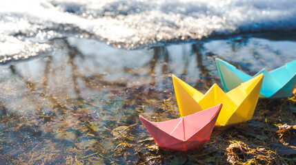 Multicolored paper boats. Colorful pink yellow blue orange ships in big spring snow puddle on winter street. Warm wet rainy weather, old grass. Hello spring, autumn. Children play, have fun outdoors