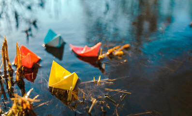 Multicolored paper boats. Colorful pink yellow blue orange ships in big spring snow puddle on winter street. Warm wet rainy weather, old grass. Hello spring, autumn. Children play, have fun outdoors