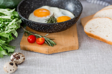 Fried eggs in a frying pan with rosemary, bread, eggs and green salad on a linen tablecloth. Breakfast, lunch and dinner. The view is soft, selective focus. Rustic style.