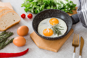 Fried eggs in a frying pan with rosemary, bread, eggs and green salad on a linen tablecloth. Breakfast, lunch and dinner. The view is soft, selective focus. Rustic style.