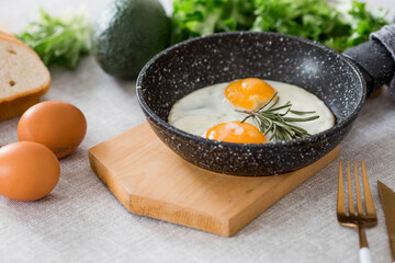 Fried eggs in a frying pan with rosemary, bread, eggs and green salad on a linen tablecloth. Breakfast, lunch and dinner. The view is soft, selective focus. Rustic style.