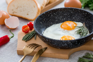 Fried eggs in a frying pan with rosemary, bread, eggs and green salad on a linen tablecloth. Breakfast, lunch and dinner. The view is soft, selective focus. Rustic style.