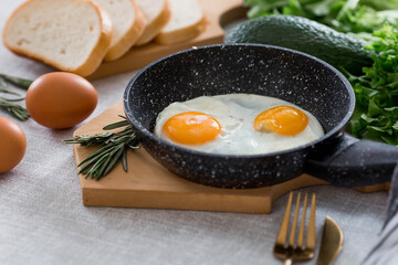 Fried eggs in a frying pan with rosemary, bread, eggs and green salad on a linen tablecloth. Breakfast, lunch and dinner. The view is soft, selective focus. Rustic style.