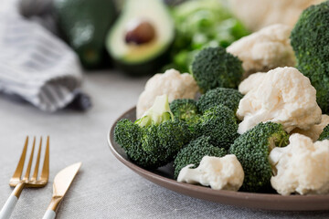 Fresh green broccoli, cauliflower and avocado on a plate on a linen tablecloth. Broccoli cabbage leaves. Light background. Vegetarian food. Healthy lifestyle.