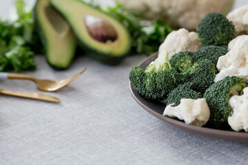 Fresh green broccoli, cauliflower and avocado on a plate on a linen tablecloth. Broccoli cabbage leaves. Light background. Vegetarian food. Healthy lifestyle.