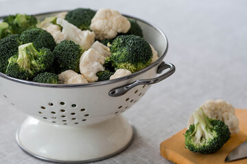 Fresh green broccoli and cauliflower in white enameled drushlak on a linen tablecloth. Broccoli cabbage leaves. Light background. Vegetarian food. Healthy lifestyle.