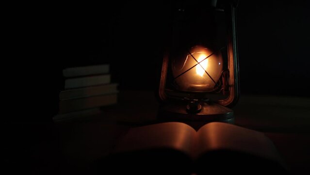 An ancient kerosene lamp, standing on the table, a book next to it, darkness around. Black background, light from a lamp