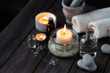 Spa setting with essential oil, candle, sea salt, pebbles, towel on dark wooden background. Massage, aromatherapy. Natural organic ingredients for relaxation, detention. Wellness in salon concept