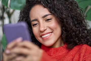 Young adult beautiful smiling latin woman looking at smartphone, happy pretty hispanic lady using...