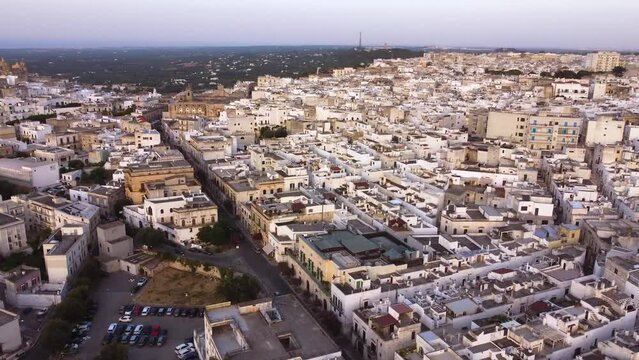 Aerial drone footage of Ostuni - La Citta Bianca (white city), Puglia, Italy at sunset. View of main street to the medieval historic old town, landmark tourist destination and new part from above.