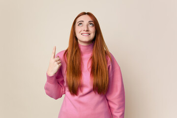 Young red hair woman isolated indicates with both fore fingers up showing a blank space.