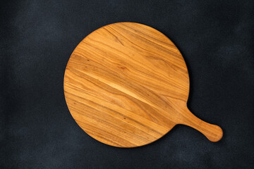 Round empty wooden charcuterie serving board with handle on old black concrete background, shabby table. Top view. Food template, copy space. Flat lay design, mockup. Layout, cooking concept, frame.