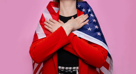 The girl in a red jacket and with an American flag hugs herself on a pink background. Concept for...