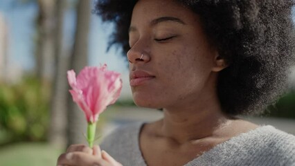 African american woman smiling confident smelling flower at park