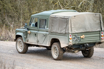British army Land Rover Defender Wolf LWB medium size utility vehicle driving along a mud track,...