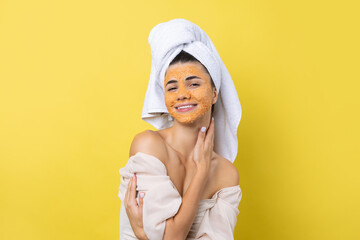 A pretty young girl with a scrub mask on her face poses for the camera and smiles against a yellow...