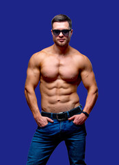 Fototapeta premium A portrait of a hot handsome strong guy man without a shirt against dark background. hands in pockets wearing glasses. Studio photo. Male beauty concept. Closeup.