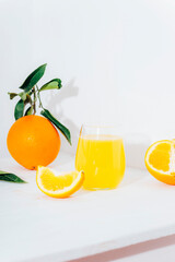 A glass of orange juice and orange fruits on white table in sunlight. Closeup