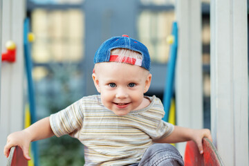 Cute two year old boy plays on playground slide on summertime. Kid play on kindergarten yard.