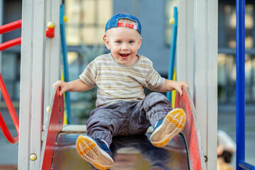 Cute two year old boy plays on playground slide on summertime. Kid play on kindergarten yard.