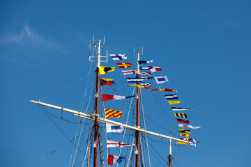 International maritime signal flags on a flagpole and masts on a sailing ship with a blue sky in the background.