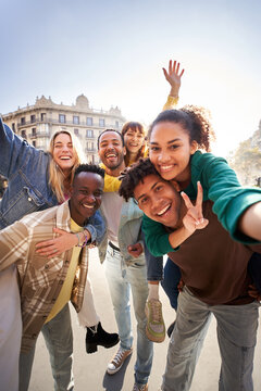 Vertical photo of a group of cheerful students college friends having fun together as they travel European city Happy community of diverse people. Selective focus on the smily couple taking the selfie