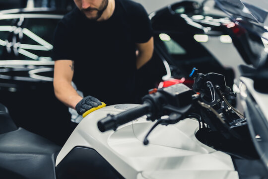 Unrecognizable car detailing expert using a sponge to deep clean white motorcycle. Indoor medium shot. Copy space. High quality photo
