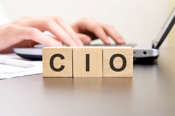 cio - acronym from wooden blocks with letters. background hands on a laptop with blur. business...