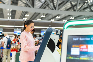 Attractive Asian woman holding passport and using self check-in kiosks machine getting boarding pass in airport terminal. People travel on holiday vacation and global airplane transportation concept.
