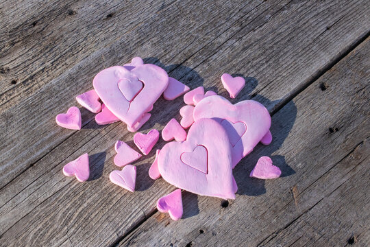 Valentine's Day studio shot of different sizes of pink clay heart shapes, the universal symbol for love and romance, arranged on a weathered old barn wood background with copy space