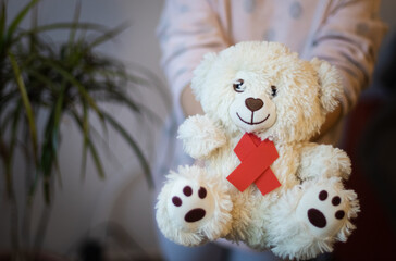 The girl holds in her hands a toy bear with a red ribbon.