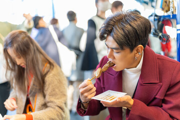 Asian man tourist eating street food grilled tuna on sticks during travel street market in Tokyo...