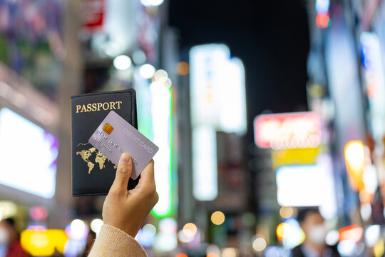 Asian Woman Hand Holding Passport And Credit Card With Crowd Of People Walking And Shopping At Shibuya, Tokyo City, Japan Background. Global Travel Transportation, Business Banking And Payment Concept